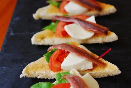Triangulo de pan/ miga tostado con montaje de rucula, tomate, queso blando y anchoa.